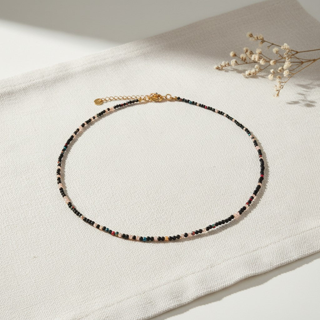 Colar Íris, gargantilha com contas de cristal facetado em tons de preto e cinza e acabamentos dourados, apresentada em cenário simples