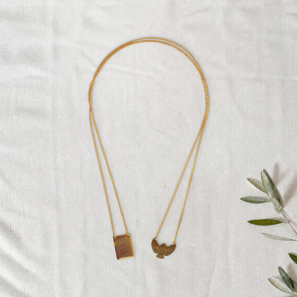 Colar Escapulário Anunciação dourado em cenário de linho com raminho de oliveira.