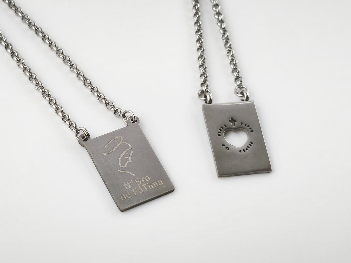 Colar Escapulário Refúgio prateado, pormenor das medalhas de Nossa Senhora de Fátima e do Sagrado Coração de Jesus.