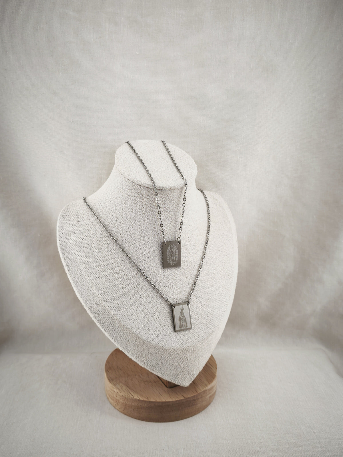 Colar Escapulário Além-Mar prateado, com medalhas de Nossa Senhora de Fátima e de Nossa Senhora de Guadalupe, apresentado em expositor.