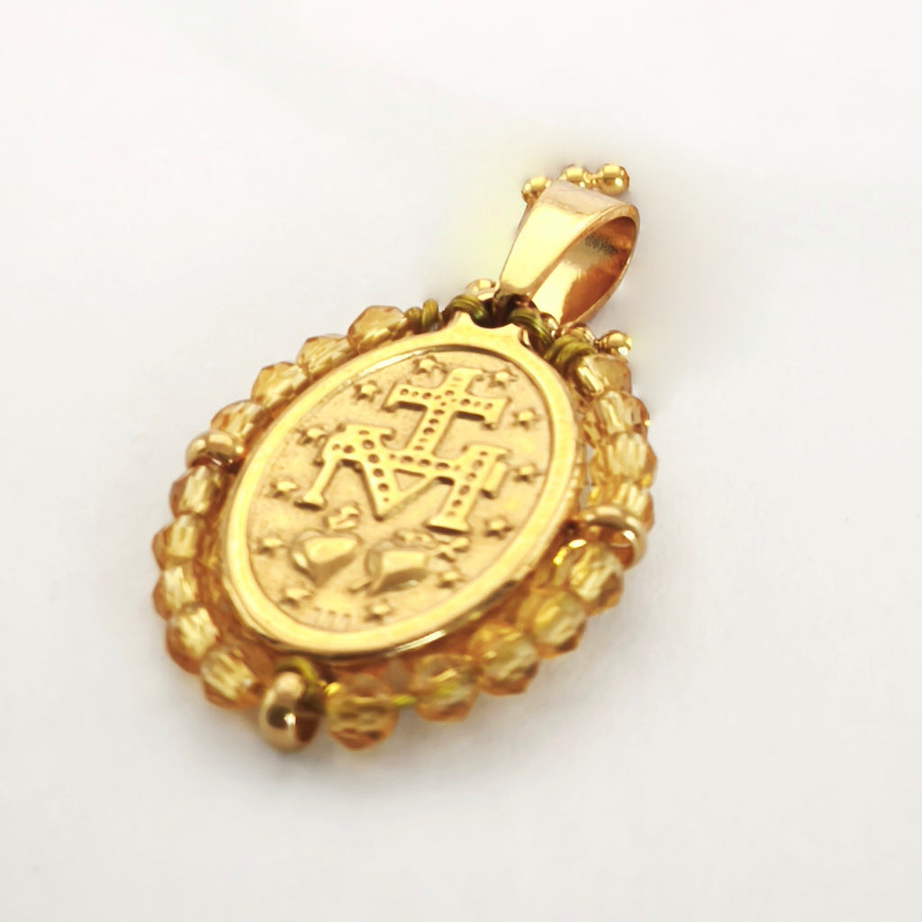 Pendente Orvalho dourado, verso da medalha rodeada de contas âmbar, com a letra M, a cruz, os dois corações e as doze estrelas.