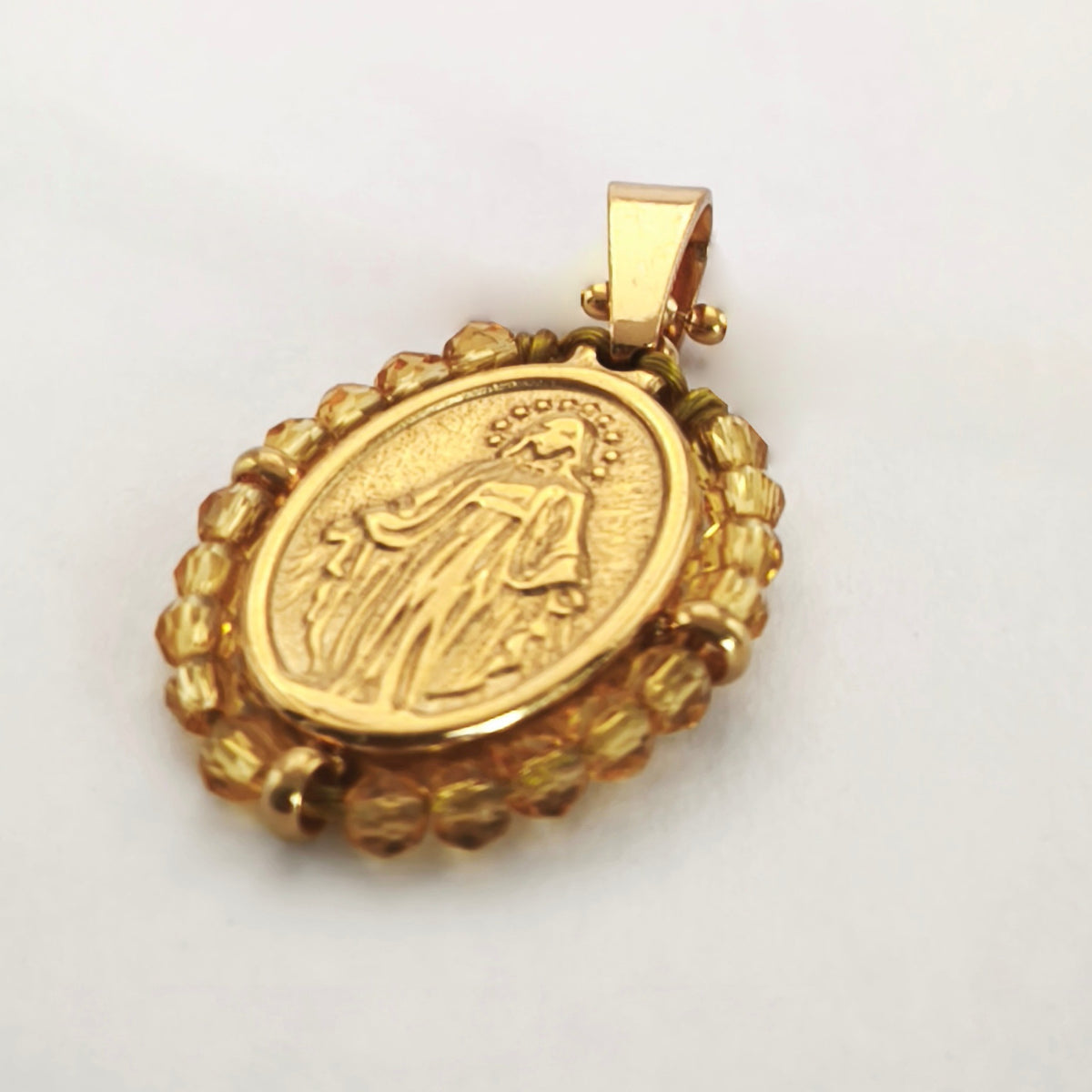 Pendente Orvalho dourado, com medalha de Nossa Senhora das Graças rodeada de contas âmbar, em perspetiva.
