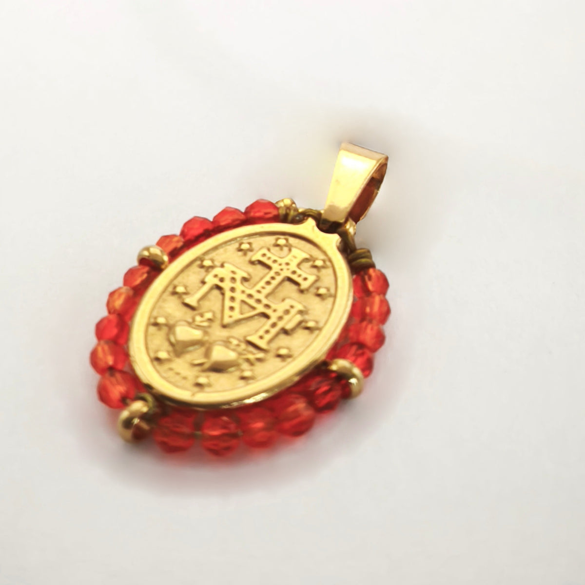 Pendente Orvalho dourado, verso da medalha rodeada de contas laranja avermelhado, com a letra M, a cruz, os dois corações e as doze estrelas.