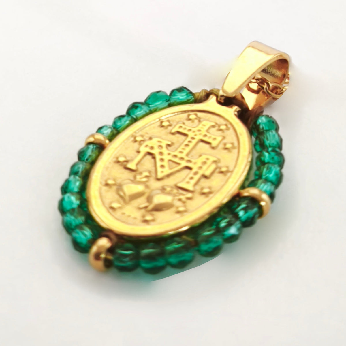 Pendente Orvalho dourado, verso da medalha rodeada de contas verdes, com a letra M, a cruz, os dois corações e as doze estrelas.
