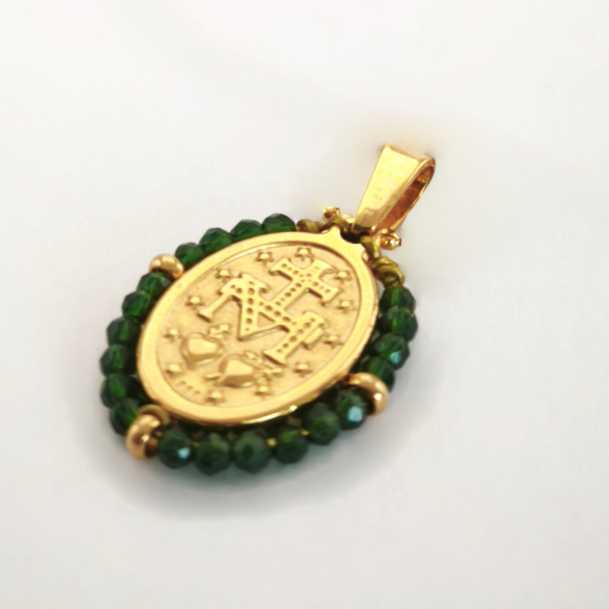 Pendente Orvalho dourado, verso da medalha rodeada de contas verde escuro, com a letra M, a cruz, os dois corações e as doze estrelas.