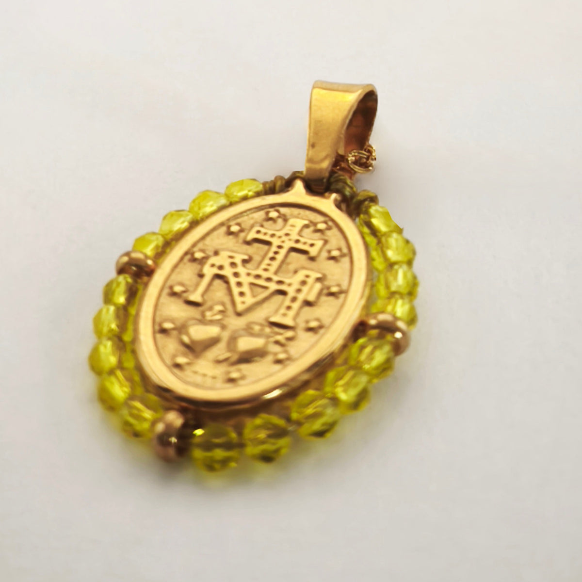 Pendente Orvalho dourado, verso da medalha rodeada de contas amarelo limão, com a letra M, a cruz, os dois corações e as doze estrelas.