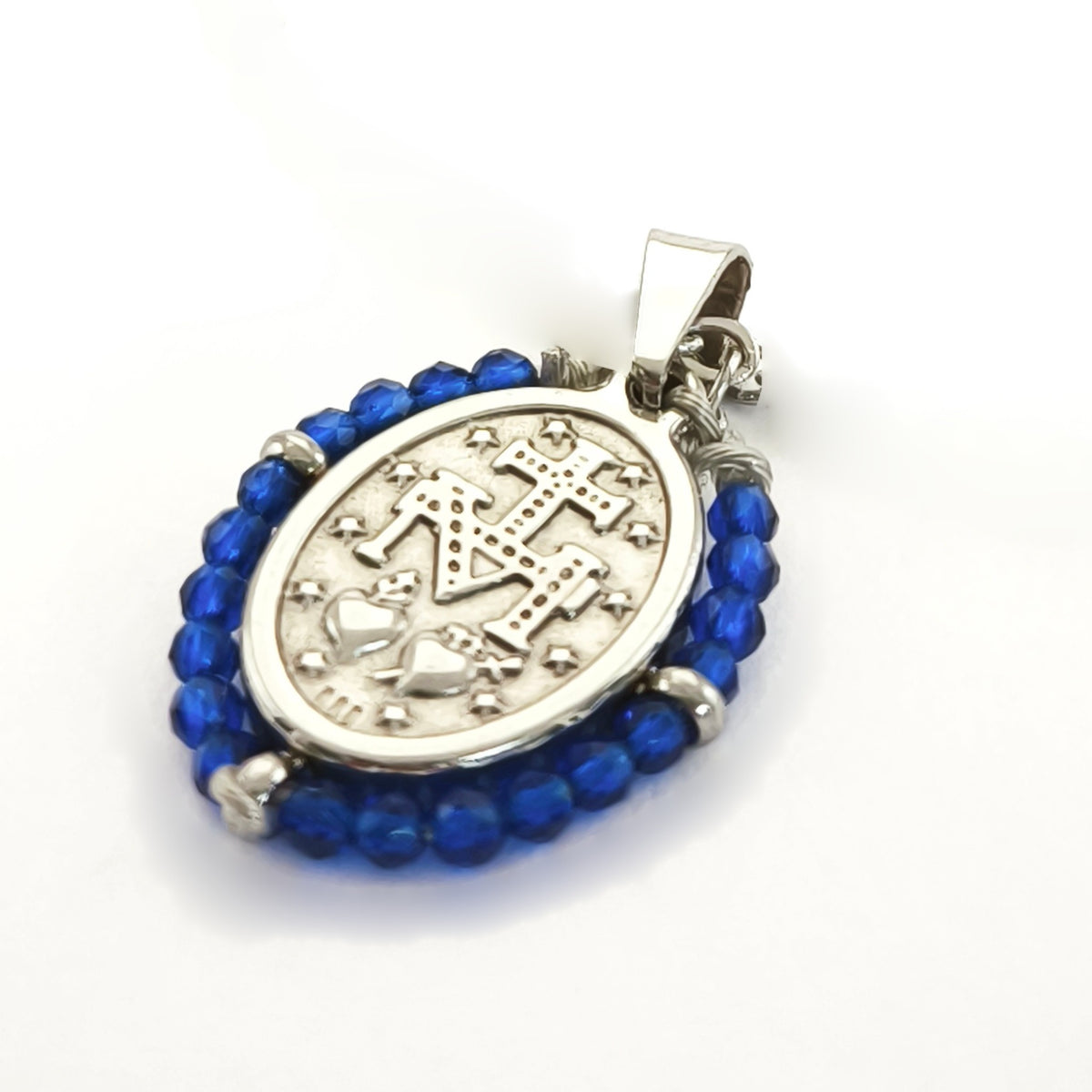 Pendente Orvalho prateado, verso da medalha rodeada de contas azul cobalto, com a letra M, a cruz, os dois corações e as doze estrelas.