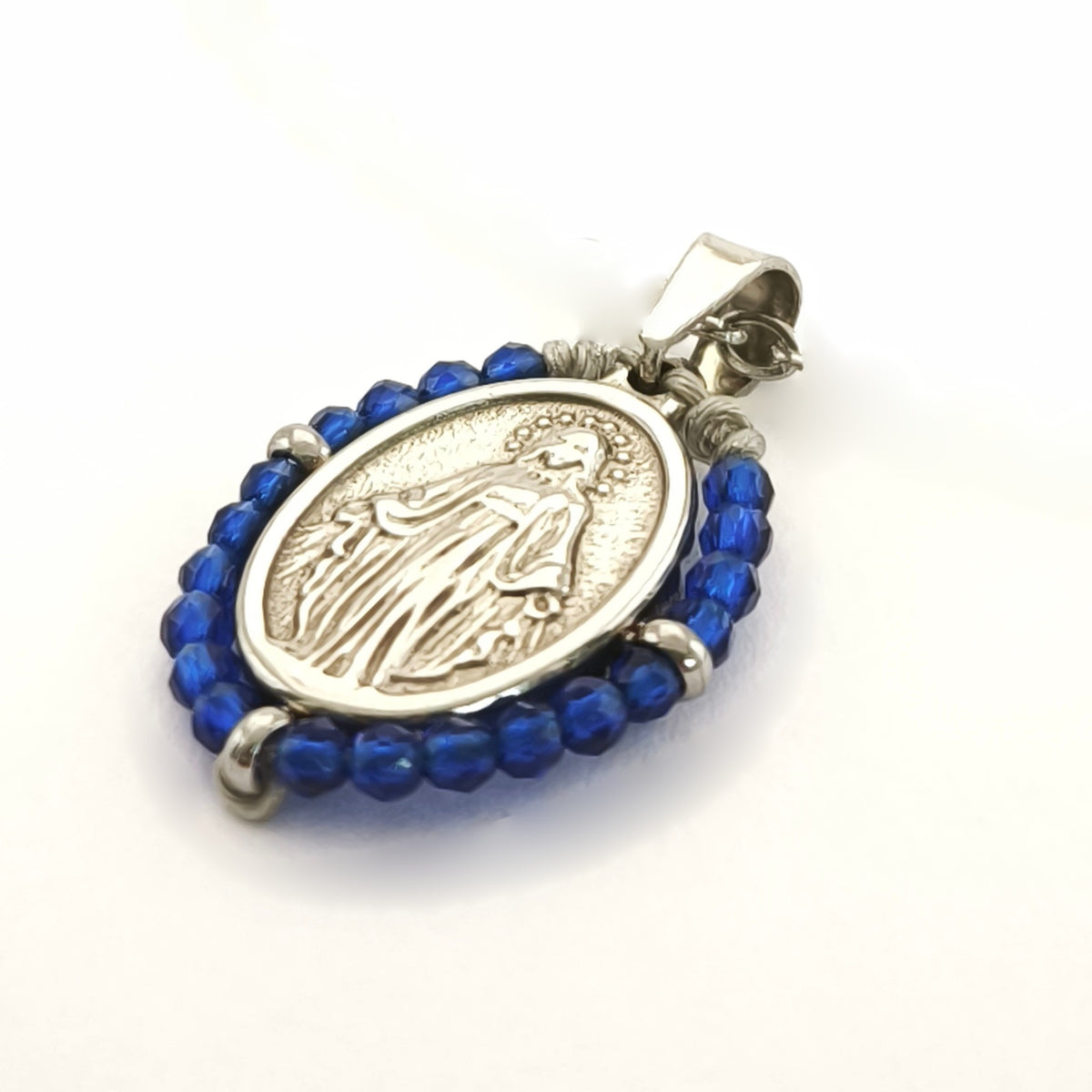 Pendente Orvalho prateado, com medalha de Nossa Senhora das Graças rodeada de contas azul cobalto, em perspetiva.