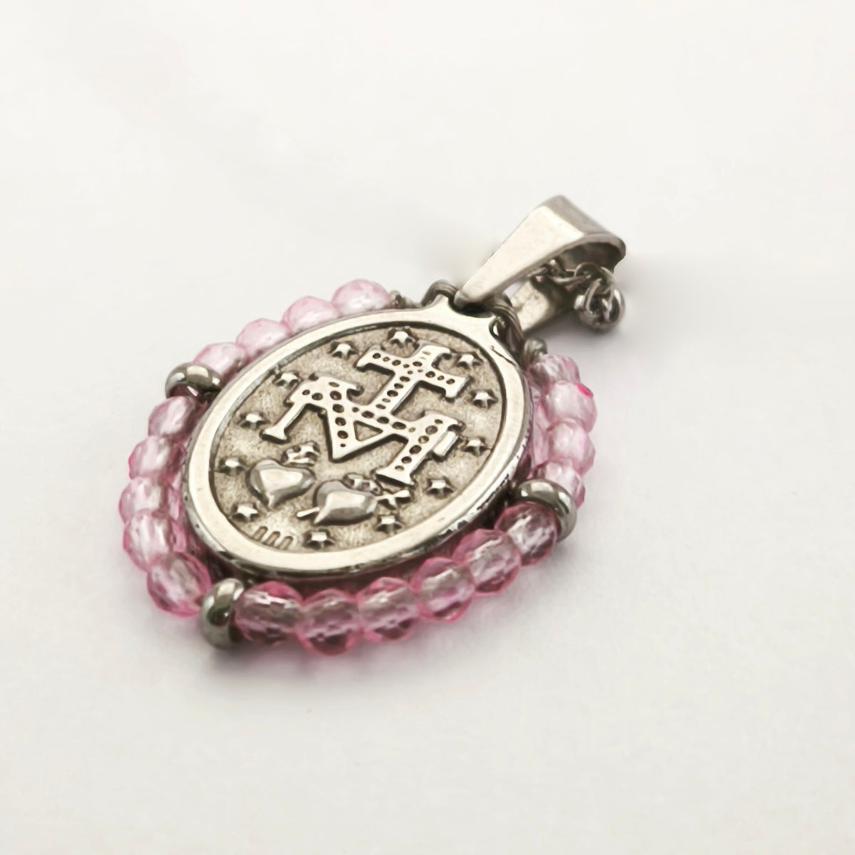 Pendente Orvalho prateado, verso da medalha rodeada de contas rosa claro, com a letra M, a cruz, os dois corações e as doze estrelas.