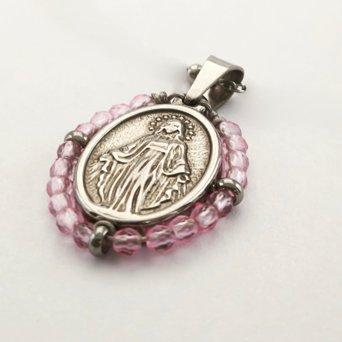 Pendente Orvalho prateado, com medalha de Nossa Senhora das Graças rodeada de contas rosa claro, em perspetiva.