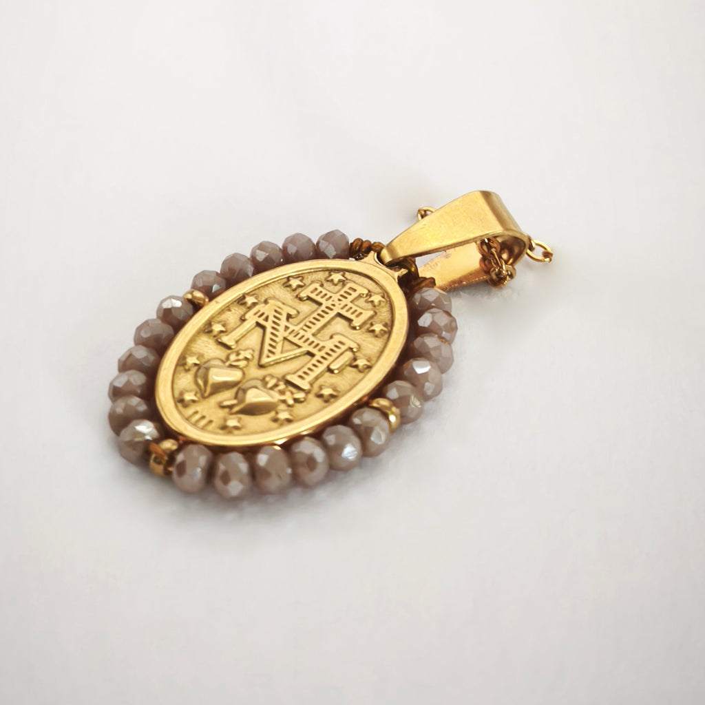 Pendente Auréola dourado, verso da medalha rodeada de contas rosa irisado, com a letra M, a cruz, os dois corações e as doze estrelas.