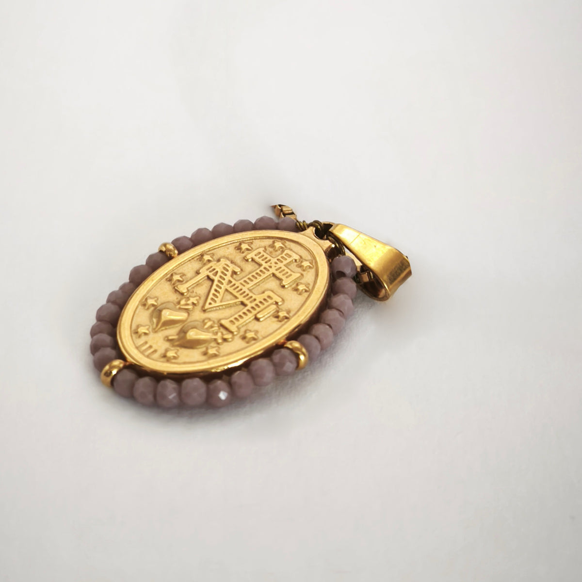 Pendente Auréola dourado, verso da medalha rodeada de contas lilás, com a letra M, a cruz, os dois corações e as doze estrelas.