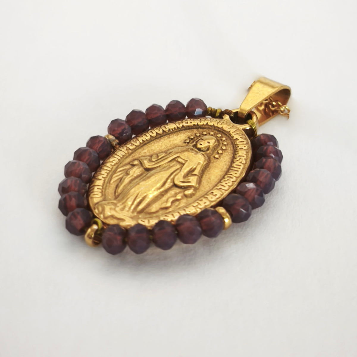 Pendente Auréola dourado, com medalha de Nossa Senhora das Graças rodeada de contas ameixa, em perspetiva.