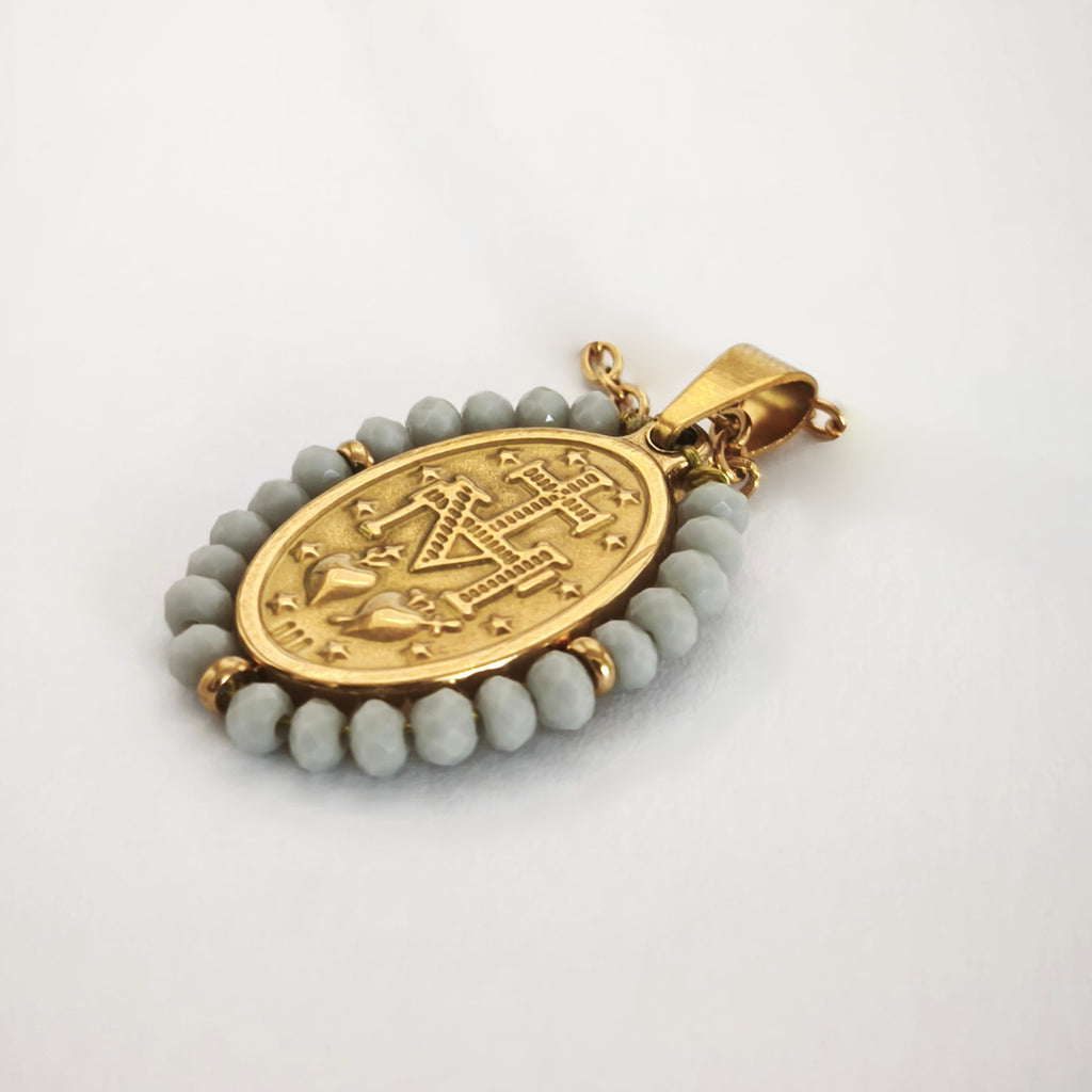 Pendente Auréola dourado, verso da medalha rodeada de contas cinza claro, com a letra M, a cruz, os dois corações e as doze estrelas.