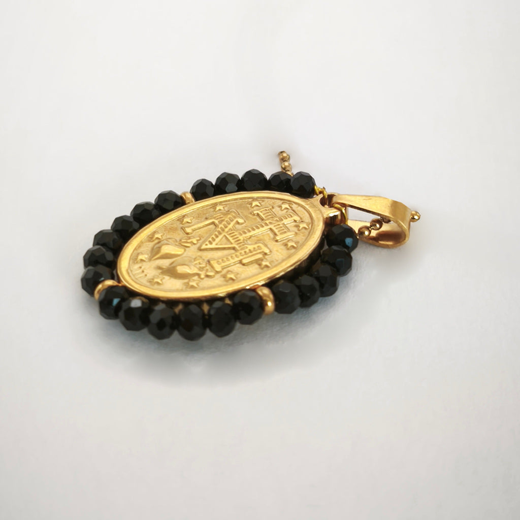 Pendente Auréola dourado, verso da medalha rodeada de contas pretas, com a letra M, a cruz, os dois corações e as doze estrelas.