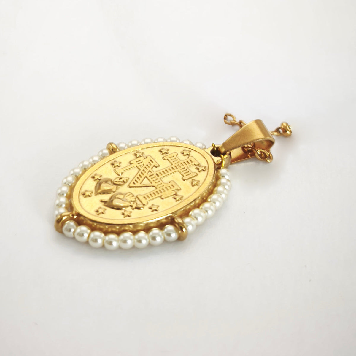 Pendente Auréola dourado, verso da medalha rodeada de pérolas artificiais miúdas, com a letra M, a cruz, os dois corações e as doze estrelas.