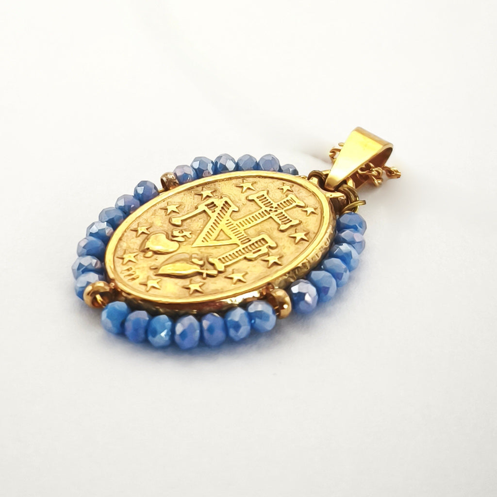 Pendente Auréola dourado, verso da medalha rodeada de contas azul céu, com a letra M, a cruz, os dois corações e as doze estrelas.