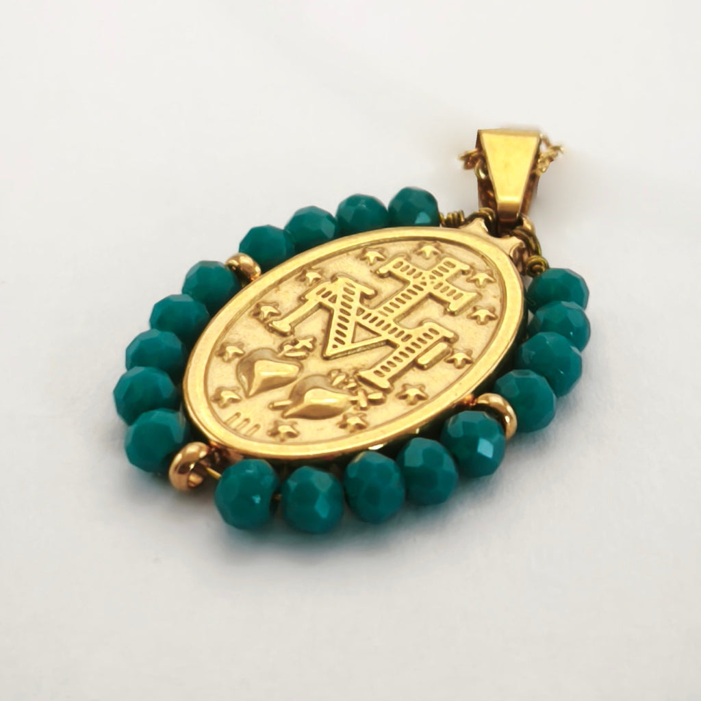 Pendente Auréola dourado, verso da medalha rodeada de contas turquesa escuro, com a letra M, a cruz, os dois corações e as doze estrelas.
