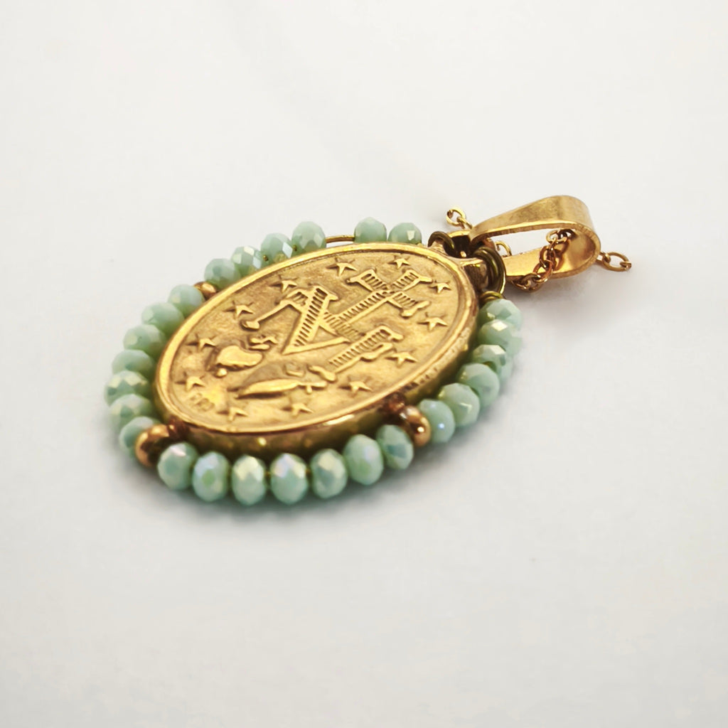 Pendente Auréola dourado, verso da medalha rodeada de contas verde-água, com a letra M, a cruz, os dois corações e as doze estrelas.