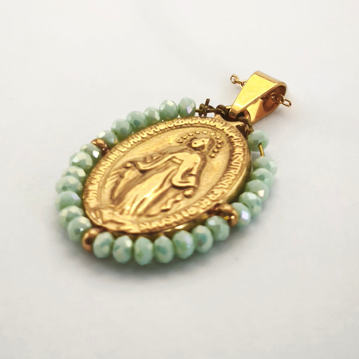 Pendente Auréola dourado, com medalha de Nossa Senhora das Graças rodeada de contas verde-água, em perspetiva.