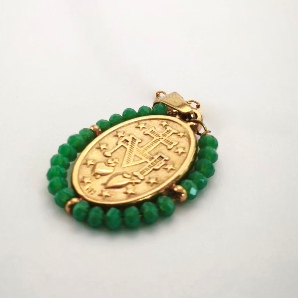 Pendente Auréola dourado, verso da medalha rodeada de contas verdes, com a letra M, a cruz, os dois corações e as doze estrelas.
