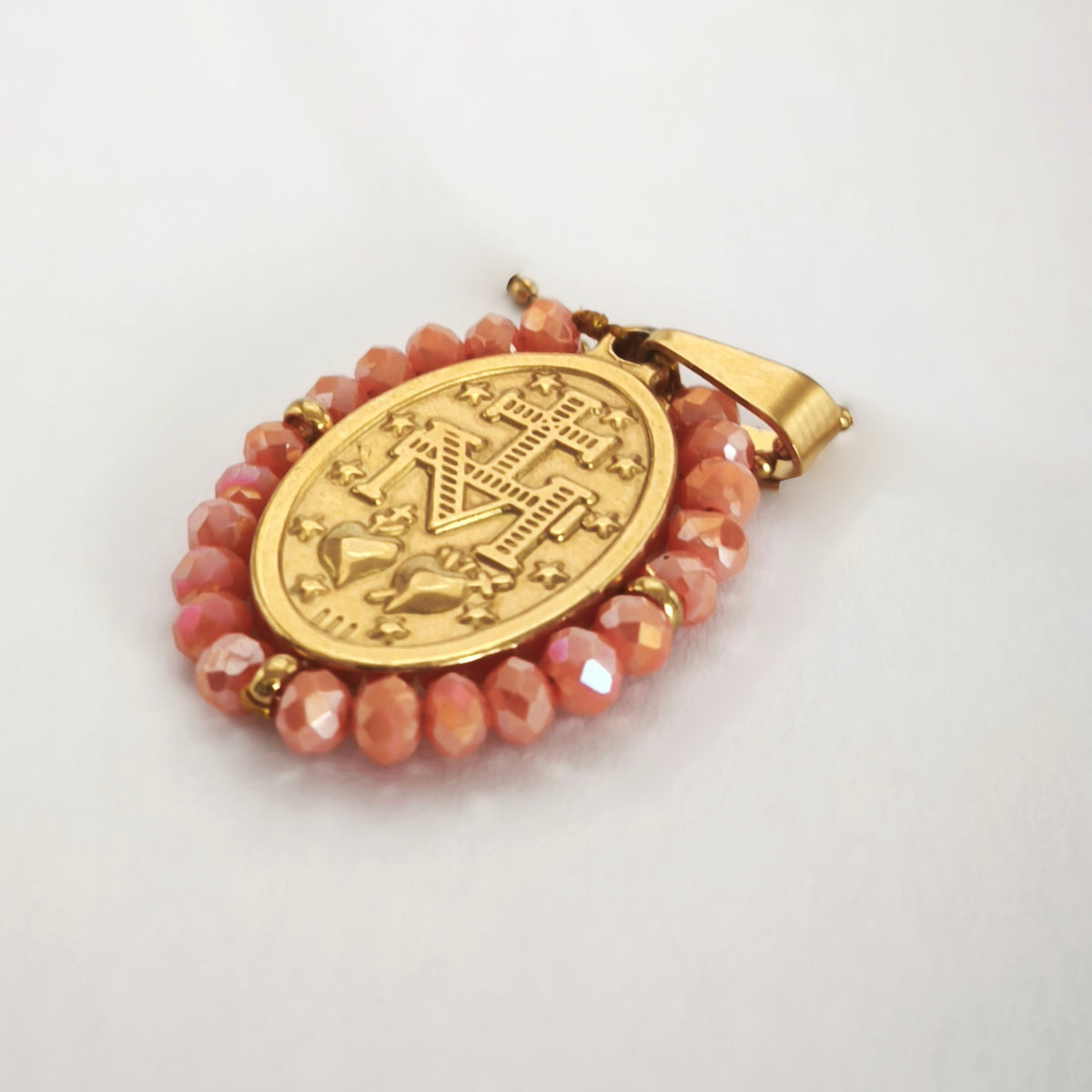 Pendente Auréola dourado, verso da medalha rodeada de contas salmão, com a letra M, a cruz, os dois corações e as doze estrelas.
