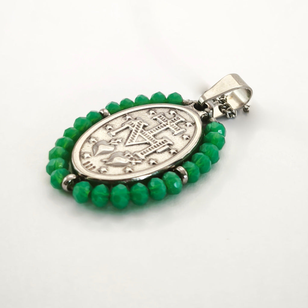 Pendente Auréola prateado, verso da medalha rodeada de contas verdes, com a letra M, a cruz, os dois corações e as doze estrelas.