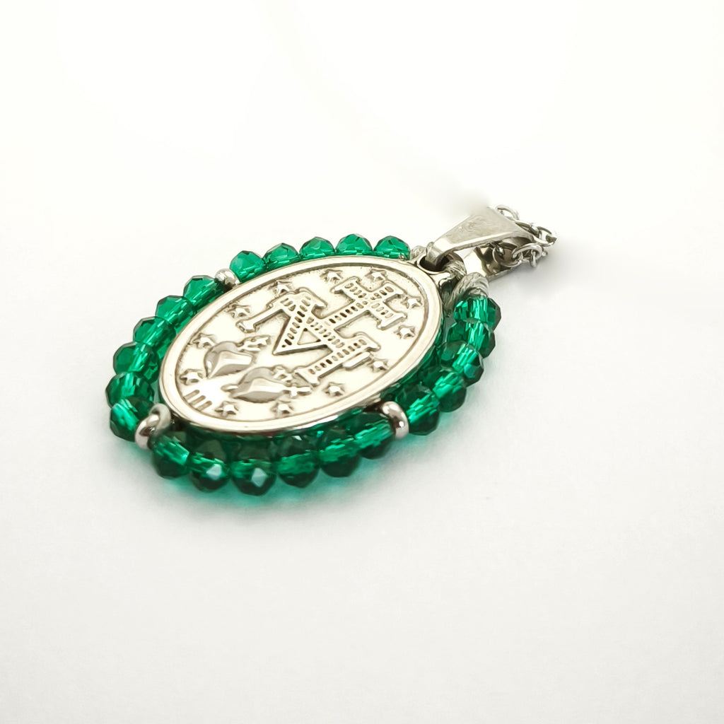 Pendente Auréola prateado, verso da medalha rodeada de contas verde esmeralda, com a letra M, a cruz, os dois corações e as doze estrelas.