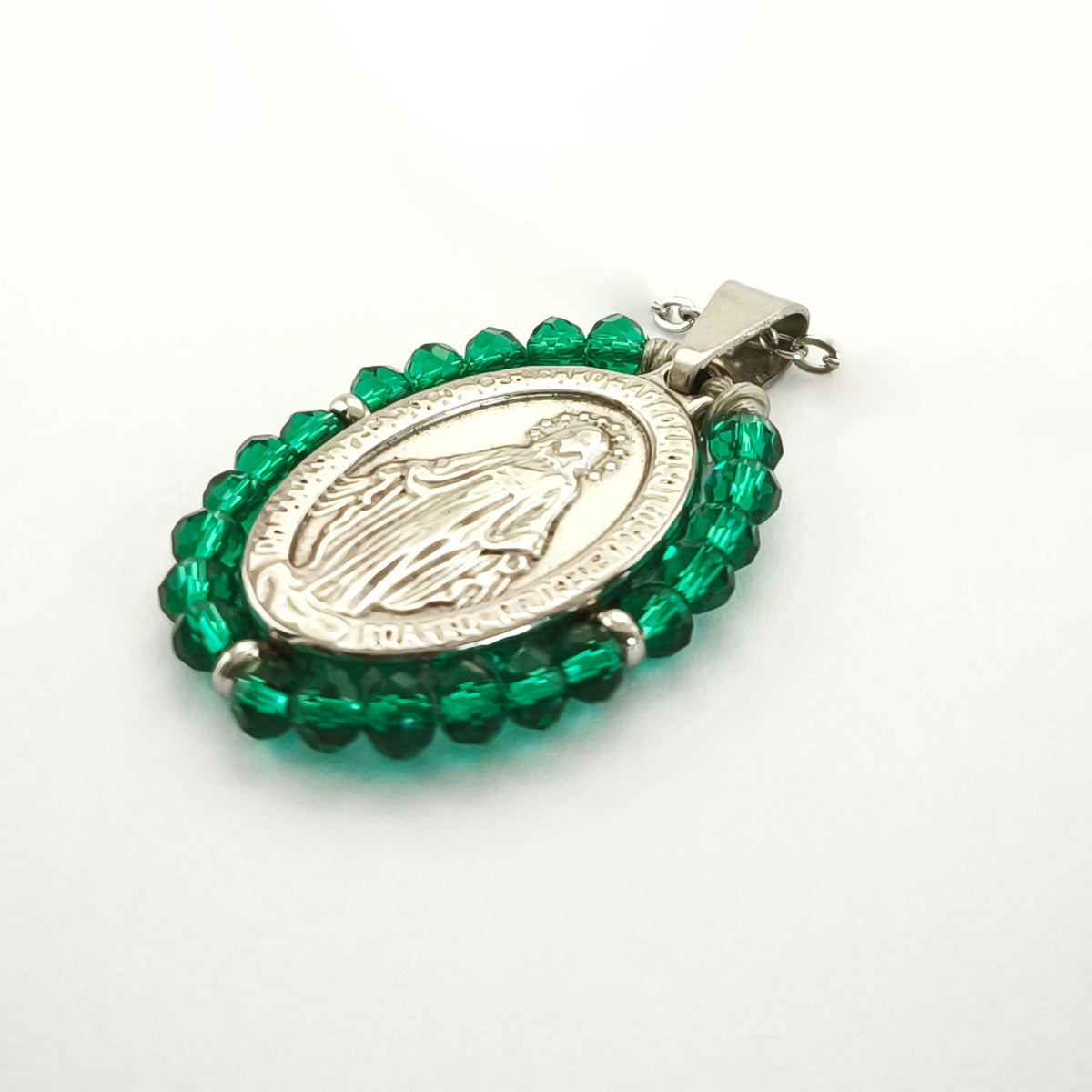 Pendente Auréola prateado, com medalha de Nossa Senhora das Graças rodeada de contas verde esmeralda, em perspetiva.