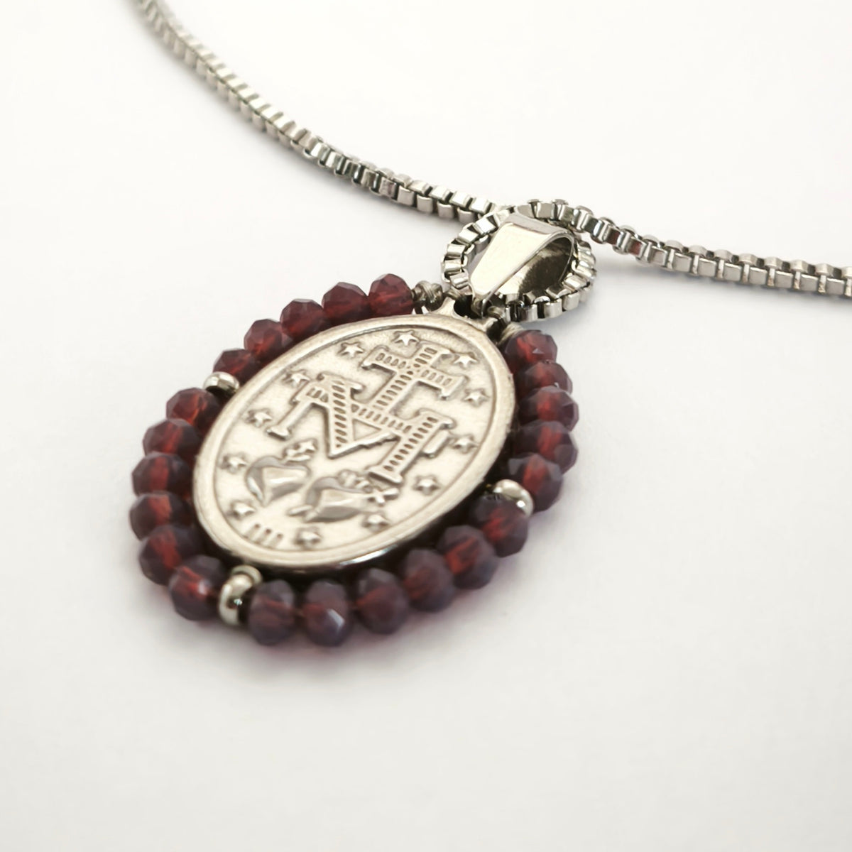 Pendente Auréola prateado, verso da medalha rodeada de contas ameixa, com a letra M, a cruz, os dois corações e as doze estrelas.