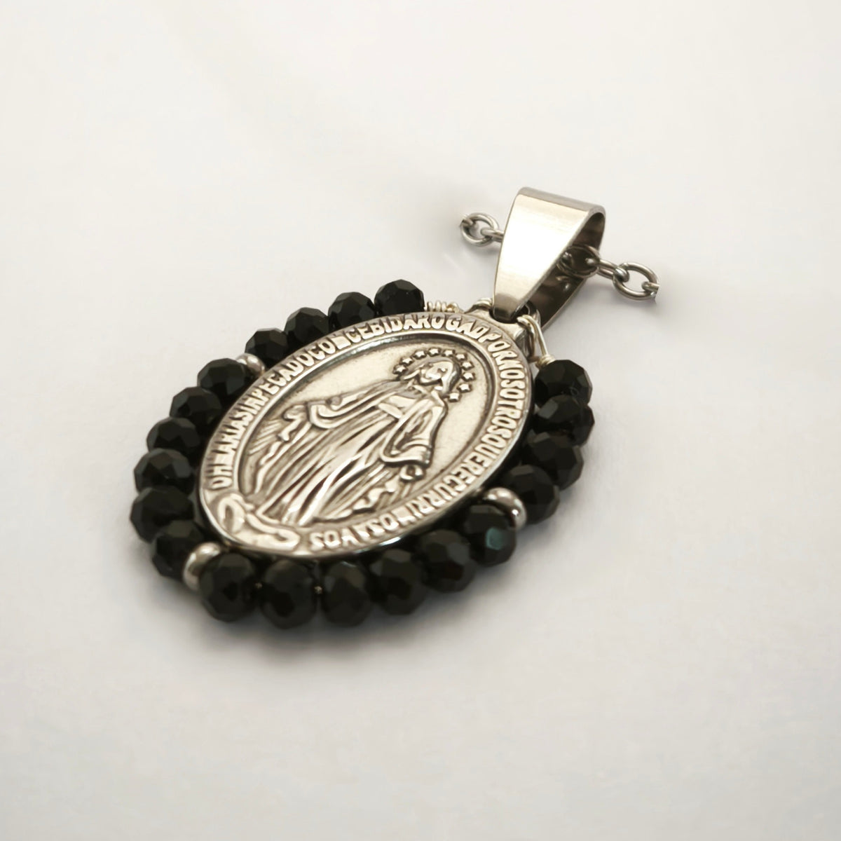 Pendente Auréola prateado, com medalha de Nossa Senhora das Graças rodeada de contas pretas, em perspetiva.